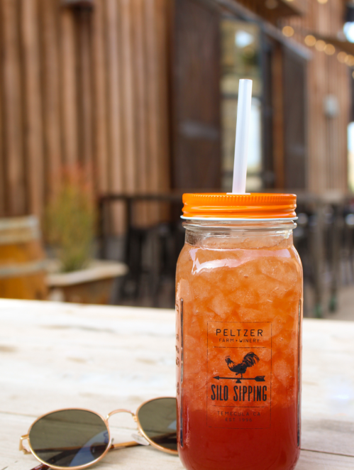 A mason jar filled with iced tea and a straw, sitting on a wooden table next to sunglasses, with a rustic background.