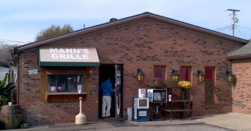 Exterior of Mann's Grille, a brick building with a green awning, featuring outdoor seating and a welcoming entrance.