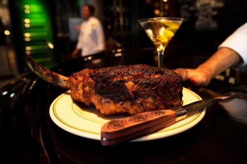 A beautifully cooked ribeye steak on a plate, accompanied by a martini with olives, set on a dark wooden table.