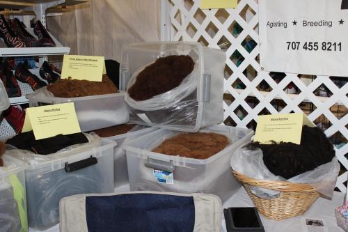 Bins of various types of wool displayed at a fair, labeled with names and contact information.