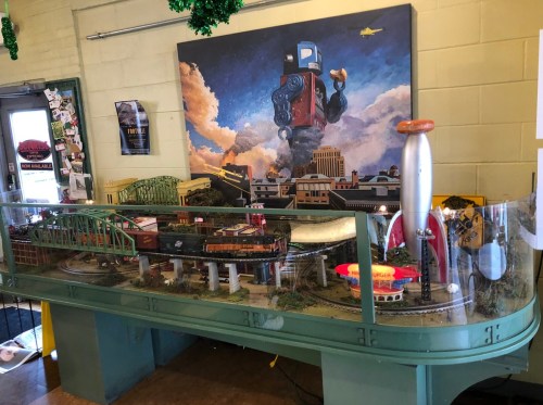 A model train display featuring various trains and a colorful backdrop of a cityscape with a robot.