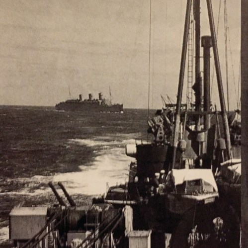 A vintage photo of a ship at sea, viewed from another vessel, with waves and a cloudy sky in the background.