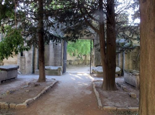 A pathway through a serene, overgrown cemetery with stone structures and trees lining the sides.