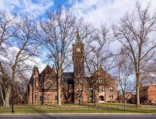 Historic building with a clock tower, surrounded by bare trees and a blue sky with clouds.