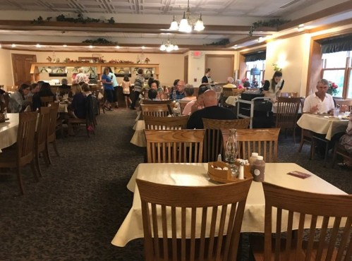A busy restaurant interior with wooden tables, diners, and staff serving in a warm, inviting atmosphere.