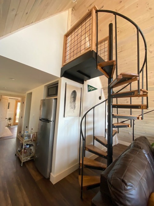 A spiral staircase leads to an upper level in a cozy, modern interior with wooden walls and a small kitchen area.