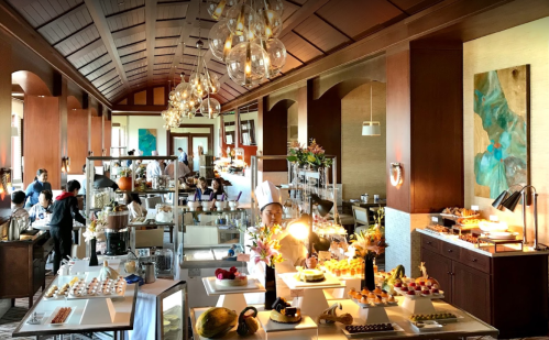 A spacious dining area with elegant decor, featuring a buffet of desserts and guests enjoying their meals.
