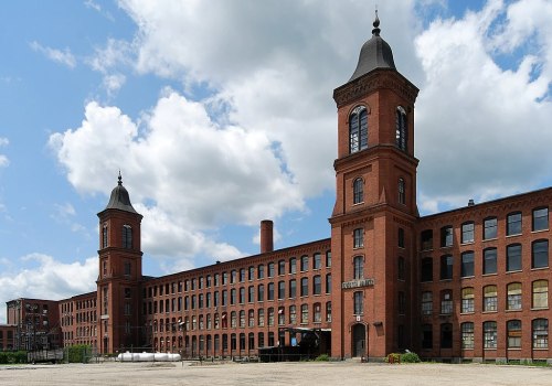 Historic red brick factory building with two tall towers under a partly cloudy sky.