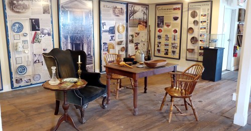 A cozy museum exhibit featuring a vintage table, chairs, and historical displays on the walls.