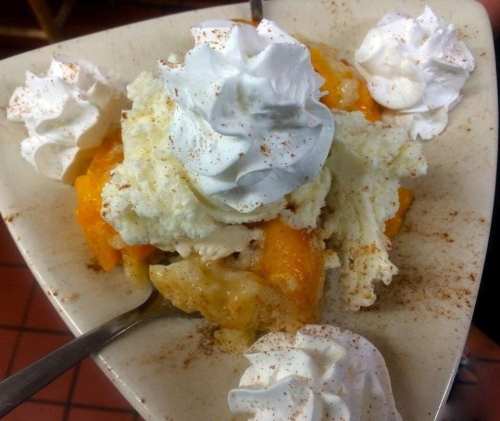 A dessert bowl with layers of fruit, whipped cream, and a sprinkle of cinnamon, served with two spoons.