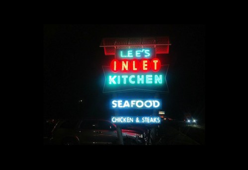 Neon sign for Lee's Inlet Kitchen, featuring "Seafood" and "Chicken & Steaks" illuminated at night.
