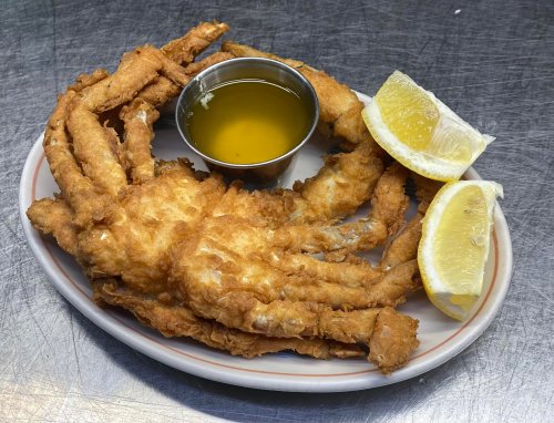 A plate of fried soft-shell crab with a small cup of dipping sauce and two lemon wedges.