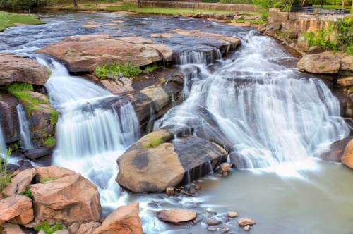 A serene waterfall cascading over rocks, surrounded by greenery and a calm pool of water below.