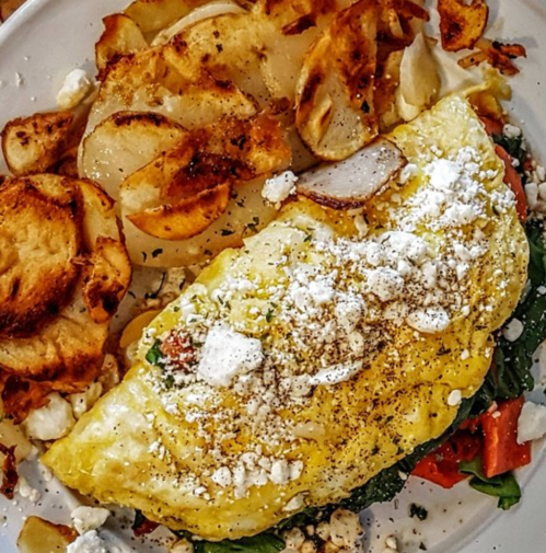 A plate featuring a fluffy omelet filled with vegetables and feta cheese, accompanied by crispy roasted potato slices.
