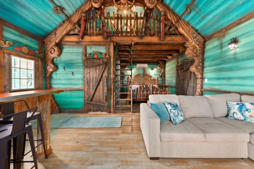 Cozy interior of a colorful cabin with wooden beams, a staircase, and a comfortable sofa.