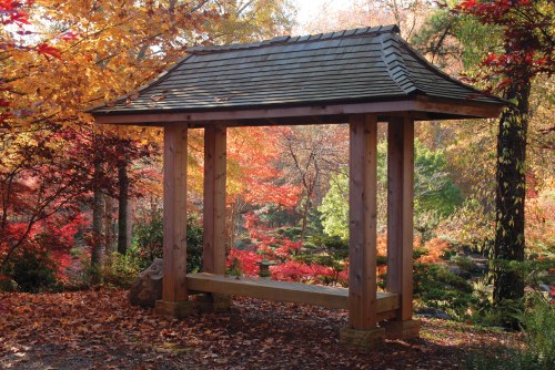A wooden pavilion surrounded by vibrant autumn foliage in a serene garden setting.