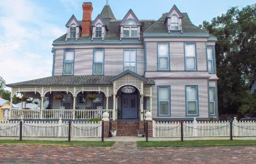 A large, Victorian-style house with a colorful facade, multiple gables, and a white picket fence.