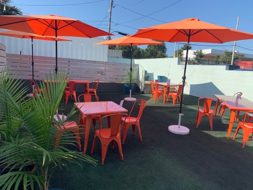 Outdoor seating area with orange umbrellas, tables, and green plants on a sunny day.