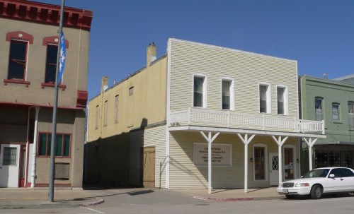 Historic buildings in a small town, featuring a yellow two-story structure with a balcony and a parked car nearby.