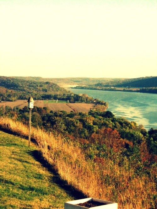 A serene river view surrounded by lush hills and greenery under a clear sky.