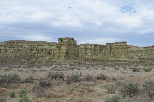 A rugged landscape featuring tall, layered rock formations under a cloudy sky, surrounded by sparse vegetation.