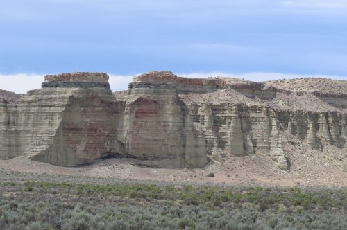 A rugged landscape featuring layered rock formations and sparse vegetation under a cloudy sky.