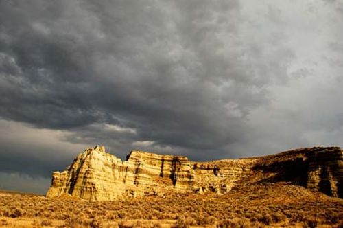 A rugged rock formation under a dramatic sky filled with dark clouds, surrounded by sparse vegetation.