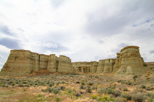 A rugged landscape featuring towering rock formations under a cloudy sky, with sparse vegetation in the foreground.