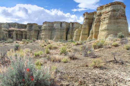 A rugged landscape featuring tall, layered rock formations and sparse vegetation under a partly cloudy sky.