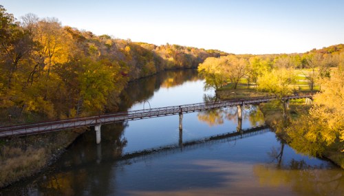 A serene river scene with a wooden bridge surrounded by vibrant autumn foliage and calm waters.