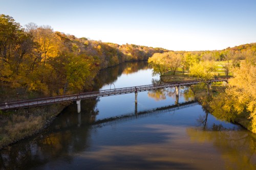 A serene river scene with a bridge, surrounded by trees in vibrant autumn colors under a clear blue sky.