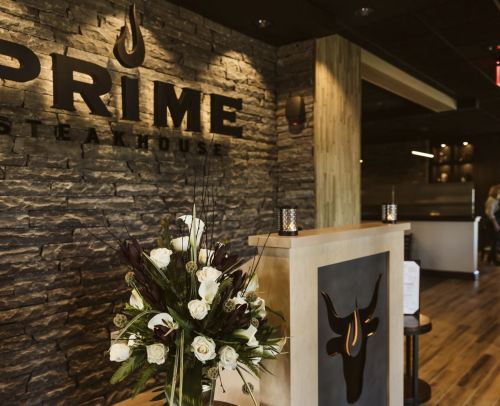Interior of Prime Steakhouse featuring a stone wall, a wooden reception desk, and a floral arrangement.