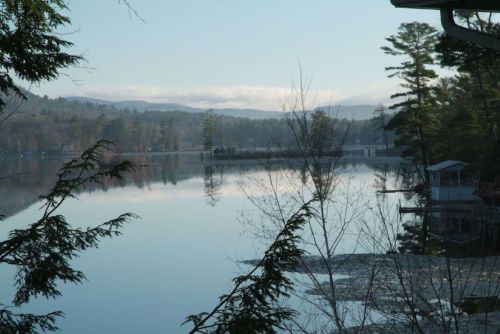 Serene lake view with misty mountains in the background, surrounded by trees and calm water reflecting the sky.