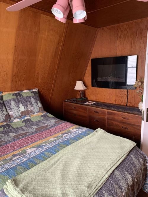 Cozy bedroom with a patterned bedspread, wooden walls, a lamp, and a TV mounted on the wall.