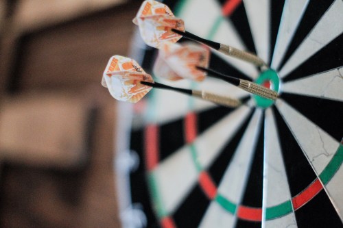 Three darts are embedded in the bullseye of a dartboard, with a blurred background.