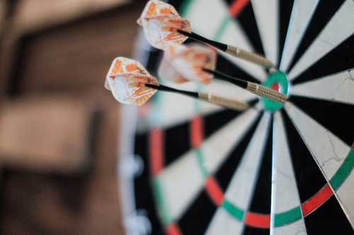 Three darts are embedded in the bullseye of a dartboard, with a blurred background.