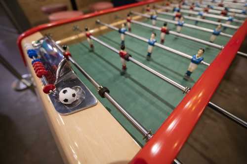 A close-up of a foosball table with players in blue and red, and a soccer ball on the side.