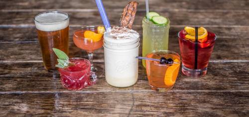 A variety of colorful cocktails and drinks arranged on a wooden table, including a beer and garnished glasses.