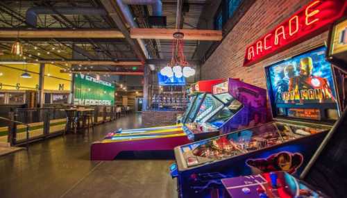 A vibrant arcade with colorful game machines, neon signs, and a lively atmosphere in a spacious venue.