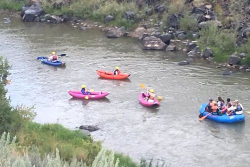 A group of people kayaking and rafting on a river surrounded by rocks and greenery.