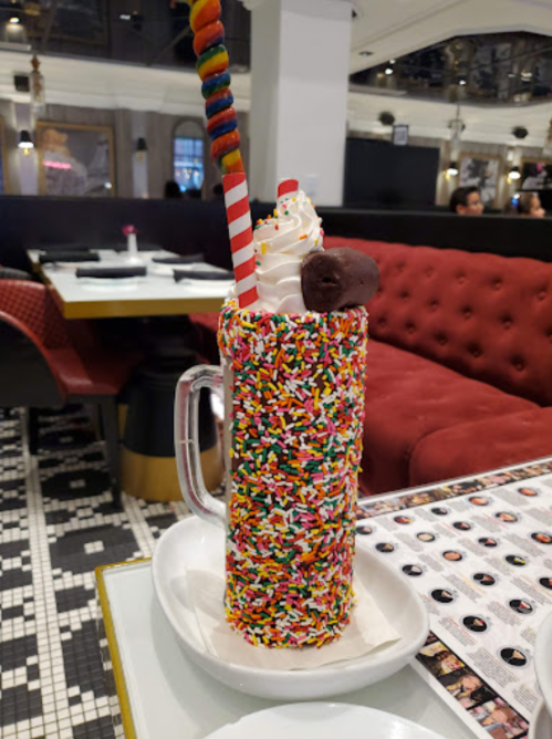 A colorful milkshake covered in sprinkles, topped with whipped cream and a cookie, served with a striped straw.