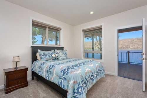 Cozy bedroom with a patterned bedspread, window views, and a door leading to a balcony overlooking a lake.