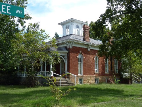 Historic red brick house with a tower, surrounded by trees and a grassy yard, near a street sign for Lee Ave.