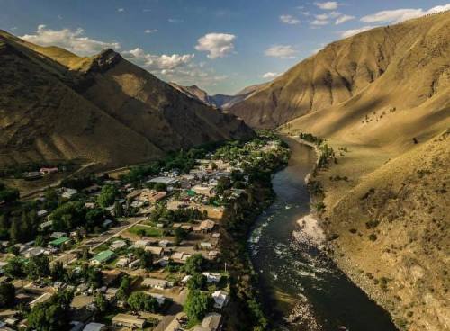 Aerial view of a river winding through a valley, surrounded by mountains and a small town with green trees and buildings.