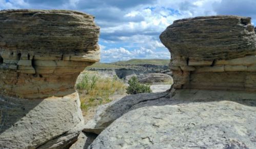 Two large rock formations stand against a cloudy sky, with a canyon visible in the background.