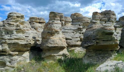 Rock formations with unique shapes surrounded by green grass under a partly cloudy sky.