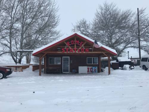 A small wooden building with a sign reading "RUM STATION," surrounded by snow and trees in a winter landscape.