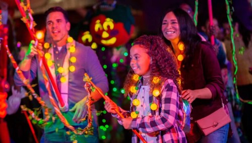 A family enjoys a festive event, wearing glowing accessories and smiling while holding colorful sticks.