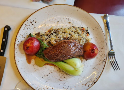 A plate featuring a piece of steak, wild rice, bok choy, and two red apples, garnished with sauce.