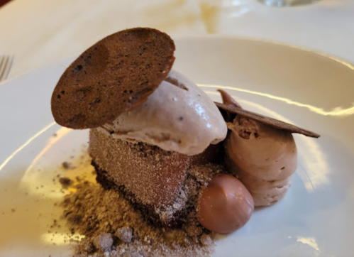 A decadent chocolate dessert with mousse, cookie garnish, and chocolate spheres on a white plate.